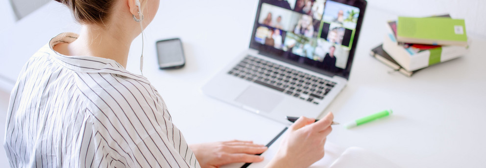 Digitales Lernen Am Schreibtisch sitzende Studentin schaut Lernvideos, daneben liegen Bücher und Stifte.